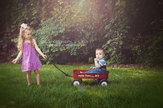 two young children pulling a red wagon in the grass