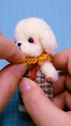 a small white teddy bear being held by someone's hand and wearing a yellow bow tie