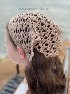 a woman wearing a crochet hat sitting on a bench next to the ocean