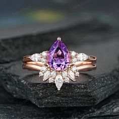 a ring with an amethorate and white diamonds on it sitting on top of a rock