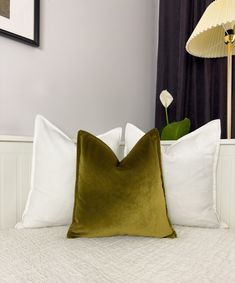 a bed with white and green pillows on top of it next to a wall mounted lamp