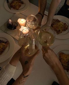 several people toasting wine glasses at a table with food and candles in the background