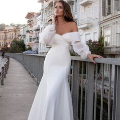 a woman in a white dress is standing on a bridge and posing for the camera