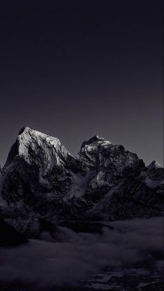 black and white photograph of the top of a snowy mountain with clouds in front of it