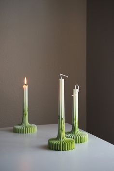 three green candles sitting on top of a white table