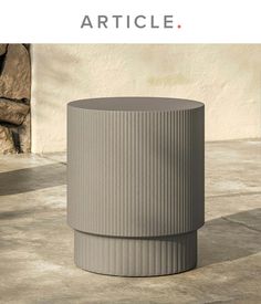 a grey vase sitting on top of a cement floor next to a stone wall with the words article written above it