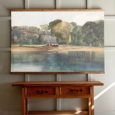 a painting hanging on the wall next to a wooden table with drawers and a bench underneath it