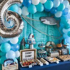 a table topped with balloons and desserts next to a shark balloon arch filled with blue and white balloons