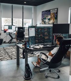 a man sitting at a desk in an office with multiple computer screens on the wall