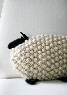 a stuffed sheep sitting on top of a white couch next to a pillow with black feet