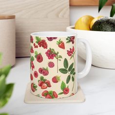 a cup with strawberries and raspberries on it sitting next to a bowl of fruit