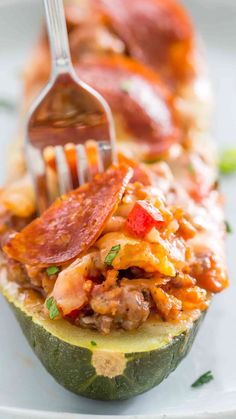 a fork is stuck into a stuffed zucchini with pepperoni and other toppings