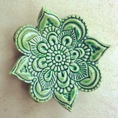 a green flower brooch sitting on top of a white table next to a wall