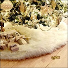 a christmas tree with presents under it in front of a pink rug and gold ornaments