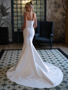 a woman in a white wedding dress standing on a tile floor with her back turned to the camera