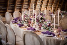 the table is set with purple flowers and candles