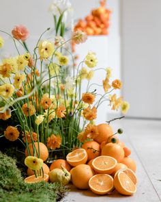 an arrangement of oranges and daffodils on the floor in front of flowers