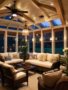 a living room filled with lots of furniture under a ceiling fan and two large windows