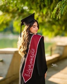 a woman wearing a graduation cap and gown with writing on the sash is standing in front of a tree