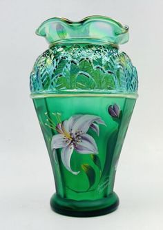 a green glass vase with flowers painted on the bottom and sides, sitting against a white background