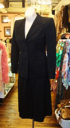 "This is a black wool gabardine suit from the early 1940's. It features a fitted jacket with medium wide notched lapels and a wide shoulder line, and a skirt with 3 inverted pleats in the front and the back. The skirt opens with a well working metal zipper. The label is from Schmitt's Clothier's in Milwaukee. The jacket is lined in black sateen. There is hand done topstitching around the lapels. I didn't find any problems or issues. It's in great condition! Comes from a smoke free home. Measurem Tailored Classic Career Skirt Suit, Classic Tailored Wool Skirt Suit, Classic Black Business Skirt Suit, Fitted Formal Uniform Suit, Classic Evening Skirt Suit With Notch Lapel, Classic Black Skirt Suit For Business, Classic Black Skirt Suit For Semi-formal Occasions, Fitted Vintage Suits For Workwear, Vintage Fitted Skirt Suit With Notch Lapel