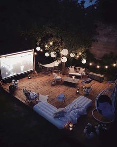 an outdoor movie is set up on a deck at night with lights strung from the trees