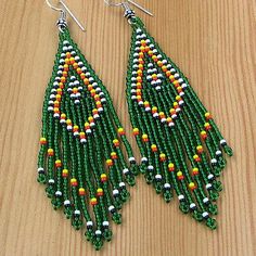 a pair of green and yellow beaded earrings sitting on top of a wooden table