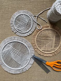 three woven coasters with scissors and yarn on the floor next to them, one is gray