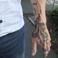 an octopus tattoo on the left wrist and right hand is shown in front of a man's arm