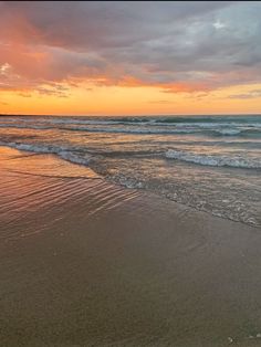 the sun is setting at the beach with waves coming in