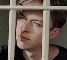 a young man looking through the bars of a jail cell, with one eye open