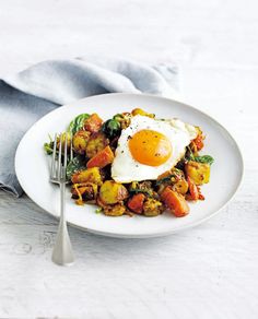 a white plate topped with fried eggs and veggies next to a silver fork