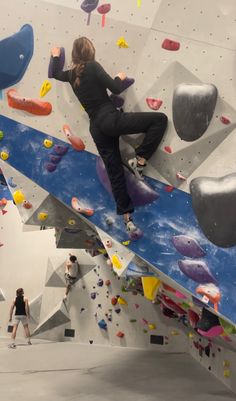 a woman climbing up the side of a rock wall with colorful rocks and boulders around her