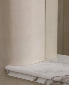 the corner of a marble counter top with a white curtain on it's side