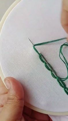 someone is stitching something on a white piece of fabric with green thread and a pair of scissors