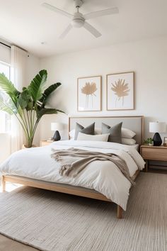 a bedroom with a bed, two plants and pictures on the wall