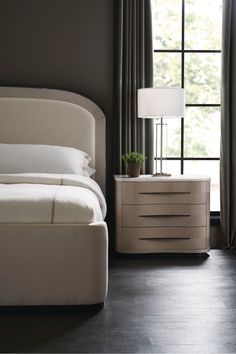 a white bed sitting next to a night stand with a lamp on top of it