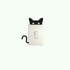 a black cat sitting in the middle of a white light switch cover with eyes drawn on it