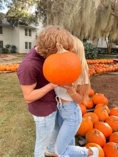 a man and woman hugging each other with pumpkins on the ground in front of them