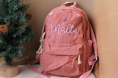 a pink backpack sitting next to a small pine tree with the word media written on it