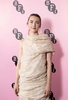 a woman standing in front of a pink wall wearing a dress with ruffles