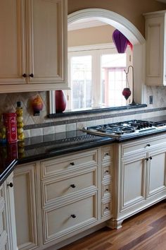 a large kitchen with white cabinets and black counter tops, an archway leading into the dining room