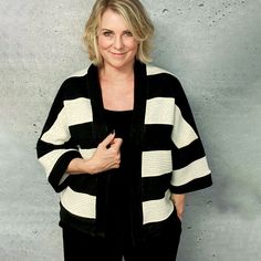 a woman standing in front of a cement wall wearing a black and white striped cardigan