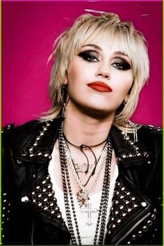 a woman with short blonde hair wearing black leather jacket and statement necklaces on her neck