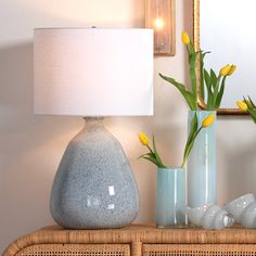 two vases with yellow flowers sit on a wicker table next to a lamp