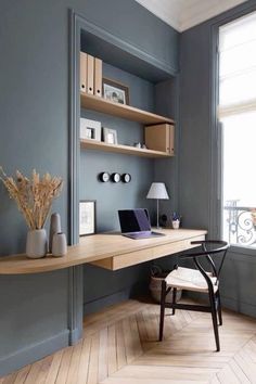 a desk with a laptop on top of it in front of a window and bookshelf