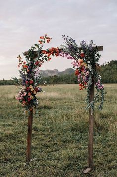 two wooden poles with flowers and greenery on them in an open grassy field,