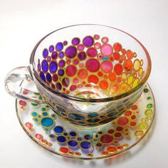 a glass cup and saucer with colorful dots on it sitting next to each other