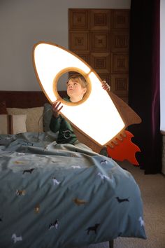 a young boy is sitting on his bed holding a light up rocket ship