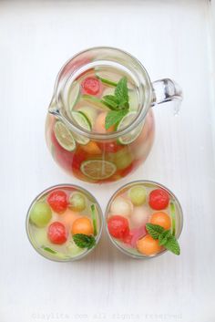 three glasses filled with water and fruit on top of a table